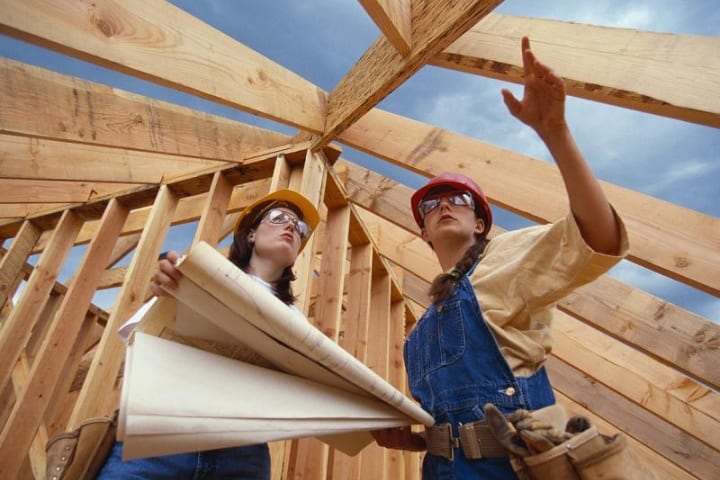 Two females working on a construction project with wooden walls in the background